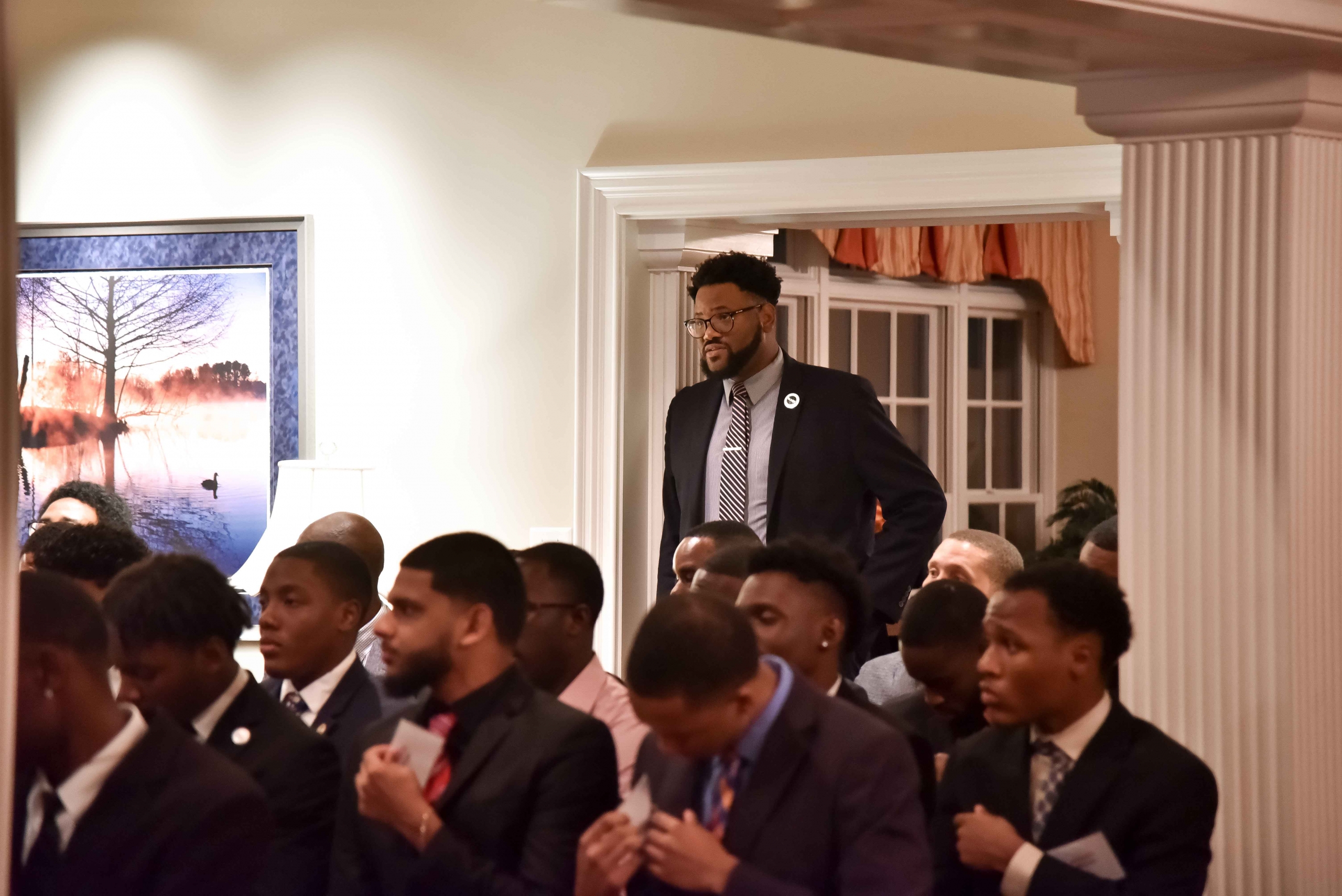 group of men sitting while one is standing, all looking off camera.