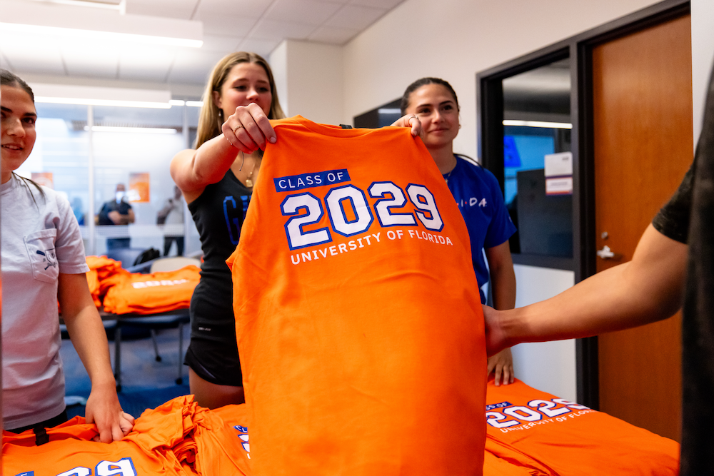 Female students smiling and handing another student their class of 2029 shirt.