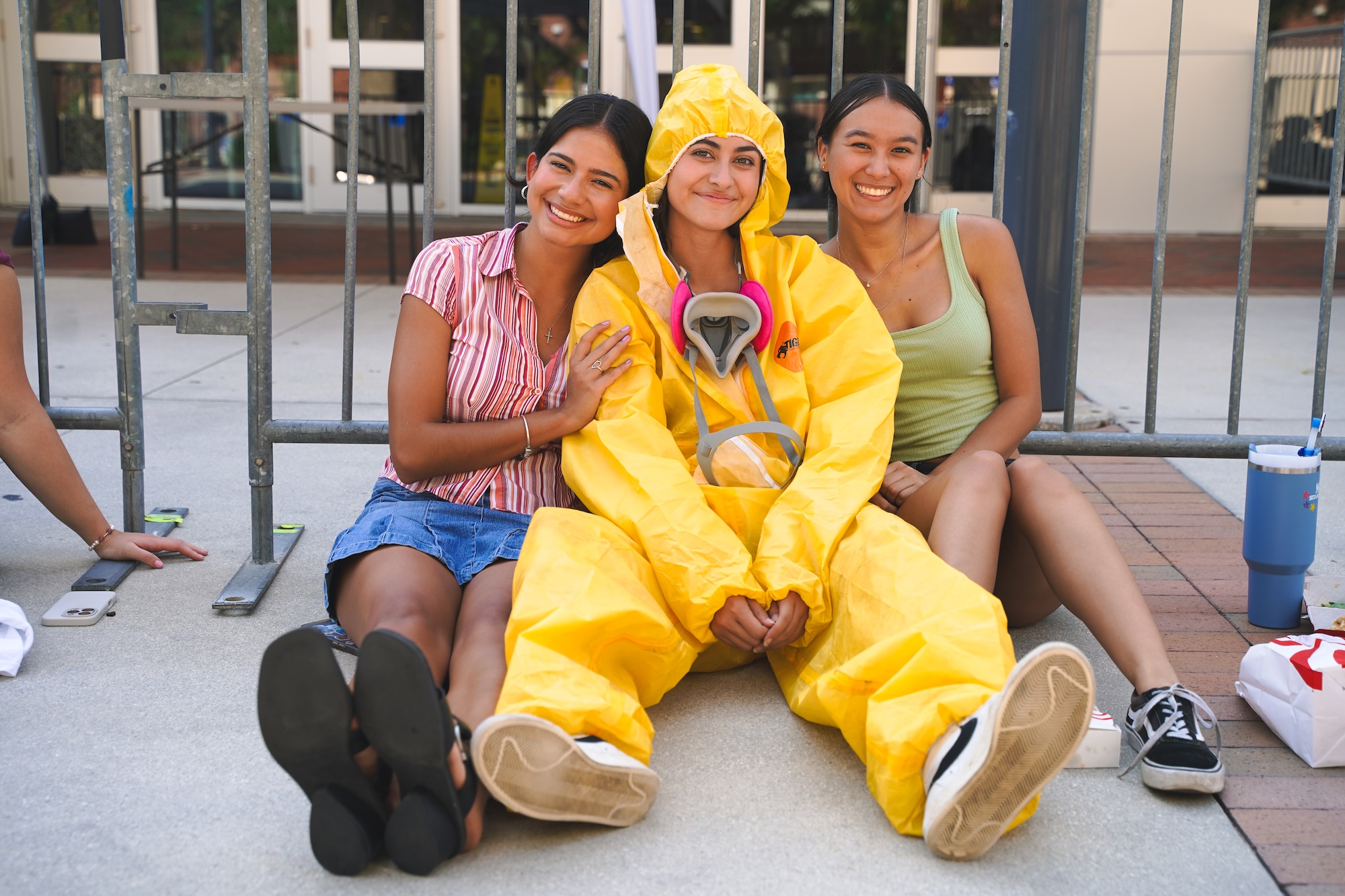 Three students smiling at the camera, one dressed in a hazmat suit for the ACCENT show with guest speaker Bryan Cranston.