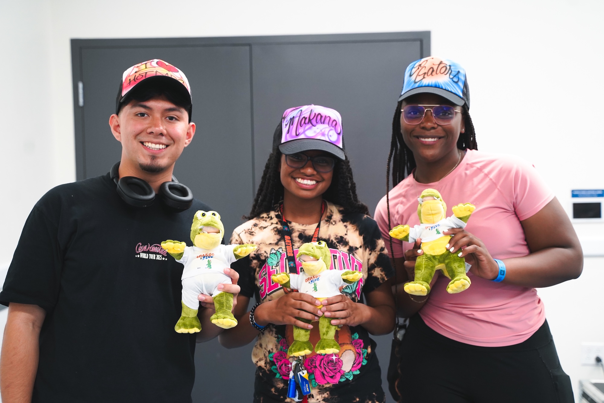Three students smiling at the camera with gator plushies and trucker hats.